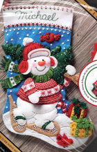 Load image into Gallery viewer, Bucilla Felt stocking kit. The design is a Snowman walking through the snow on snow shoes while holding freshly cut Christmas tree. Cardinals and wrapped gifts in the background.