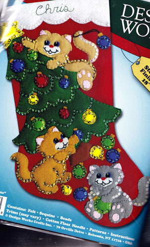 Design works christmas felt stocking kit. The design features 3 cats playing with a christmas tree while knocking off ornaments. The cats are  solid orange, tan, and gray. 