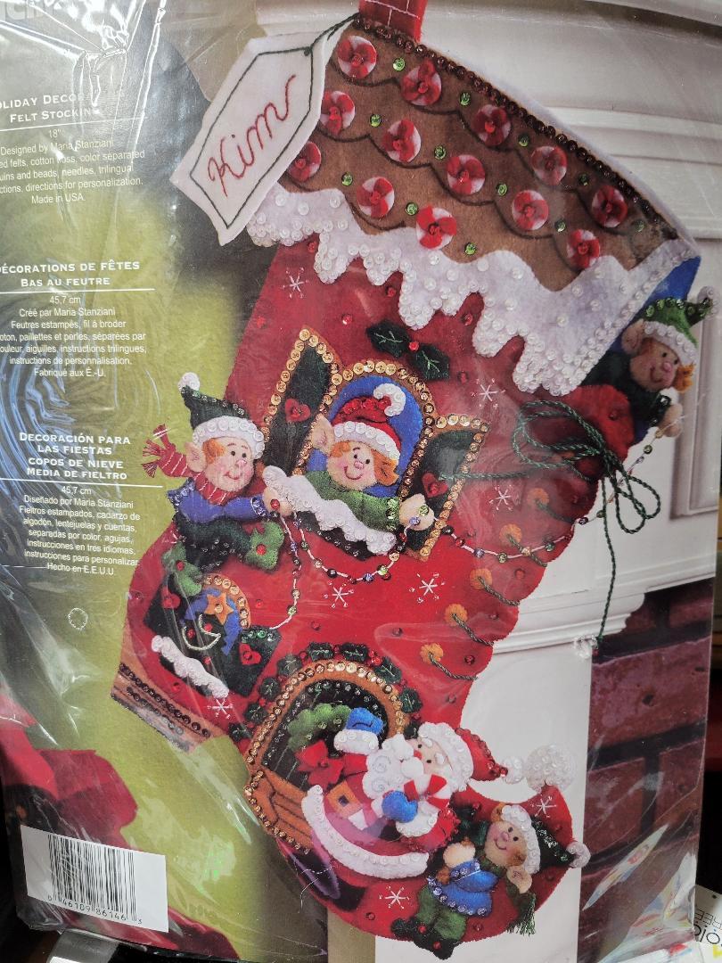 Bucilla christmas Felt stocking kit. Design features an elf house shaped like a big red boot. The elves are decorating their house with santa helping.
