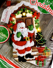 Load image into Gallery viewer, Bucilla felt stocking kit. Design features santa  with his pack of toys on a decorated front porch. This stocking kit lights up.