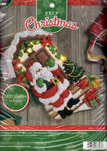 Load image into Gallery viewer, Bucilla felt stocking kit. Design features santa  with his pack of toys on a decorated front porch. This stocking kit lights up.